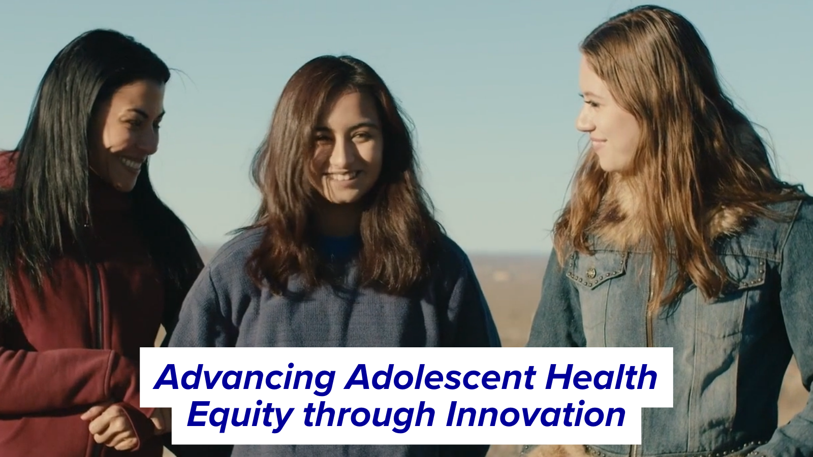 Video still of two youth and one adult walking and smiling during a conversation in a field.