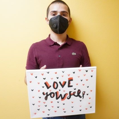 Angel, youth, holds colorful sign with hand-drawn hearts and statement: Love Yourself.